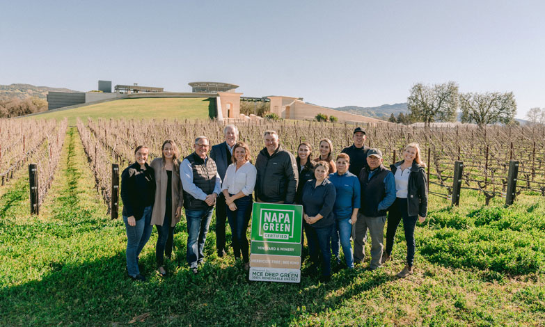 The Opus One team with the Napa Green sign mentioning our sustainability certification, for the vineyard and winery, being herbicide and bee free, and using MCE deep green energy. The vines and winery are in the background.